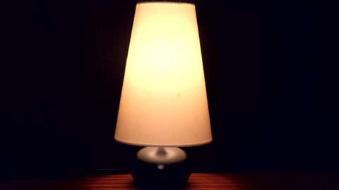 Bedside lamp on black background. Caucasian male hand  successively turns the lamp on and off with a switch.