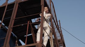 young woman looks down standing on ladder ground and leaning on handrail against boundless sky slow motion low angle shot