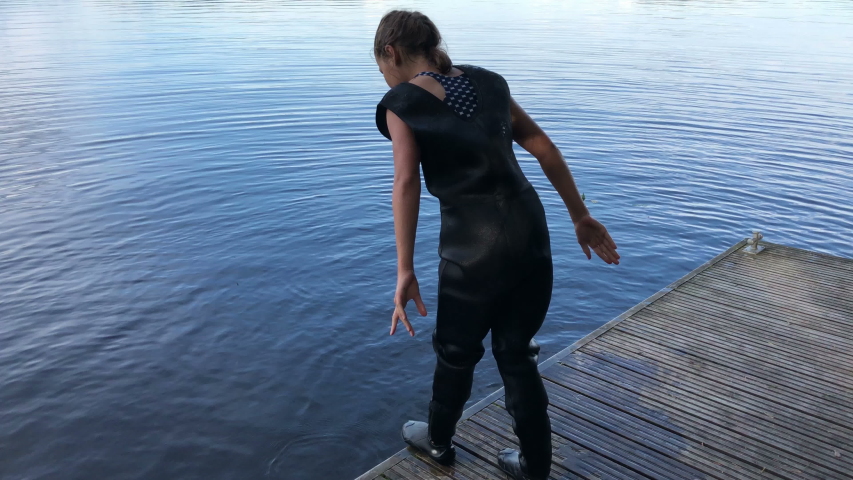 Teenage girl preparing to jump water fro pier, dressed rubber diving suit