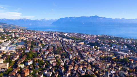 Aerial shot overflying Lausanne city descending towards train station, with Lake Leman and the Alps in background, Switzerland. Helicopter aerial shot.