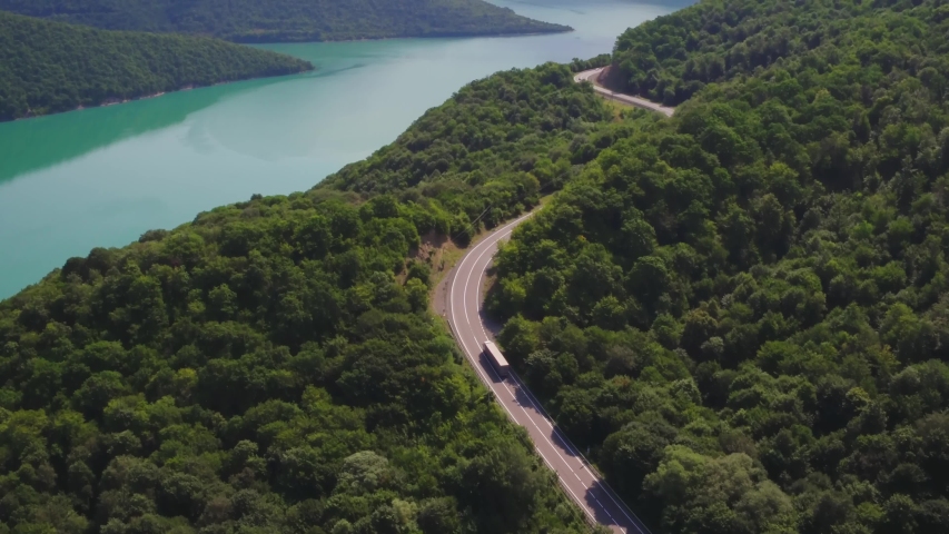 One Semi Truck with clean white trailer and red cab driving along the freeway amidst a dense forest in the mountains. Summer, sunny / Aerial footage Royalty-Free Stock Footage #1039590248
