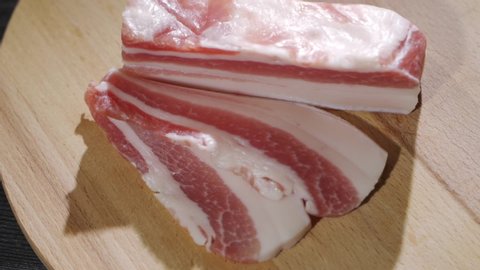 Chef cuts pieces of raw bacon by sharp knife on the wooden board