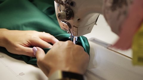 Closeup of a young woman's hands with manucure sewing green fabric with a sewing machine. Women's hands sew on a sewing machine. Fashion, creation and tailoring. High angle view