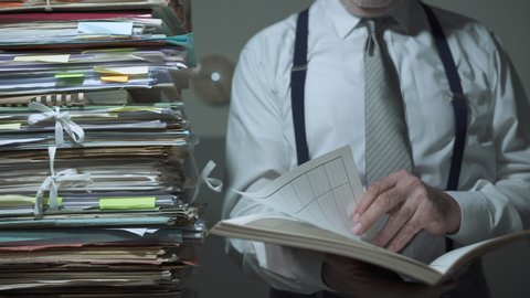 Corporate businessman overloaded with paperwork, he is reading a file and browsing pages