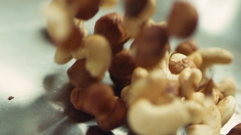 Closeup nuts frying on metal pan in slow motion. Closeup hazel nuts roasting on frying pan. Close up hazel and cashew nuts mixing in slow motion.