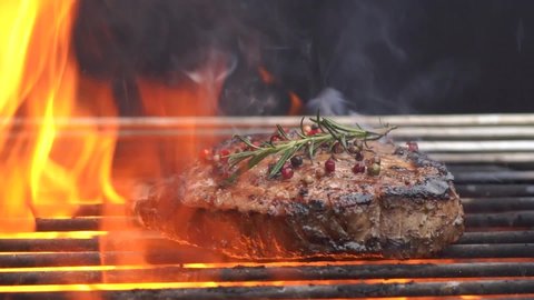 Cooking meat cutlet and  Rosemary Pepper  Salt  on hot grill barbecue grate with fire flams and smoke on black background.
