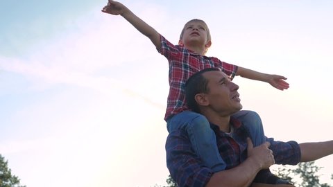 happy family father son concept. Father giving son ride on back in nature outdoors . Portrait lifestyle of happy father giving son ride on his shoulders and looking up. Cute boy with a dad playing