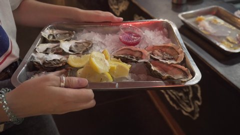 Fresh oysters on a tray with ice, sauce and lemon in the hands of a young girl. Close-up shot.