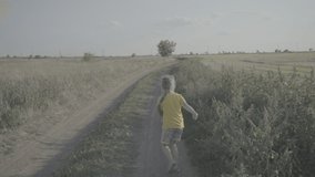 A girl runs along the road in the field. Funny girl in a yellow T-shirt is having fun. Rural dirt road. Summer holidays. No color grading. Childhood. Family video.