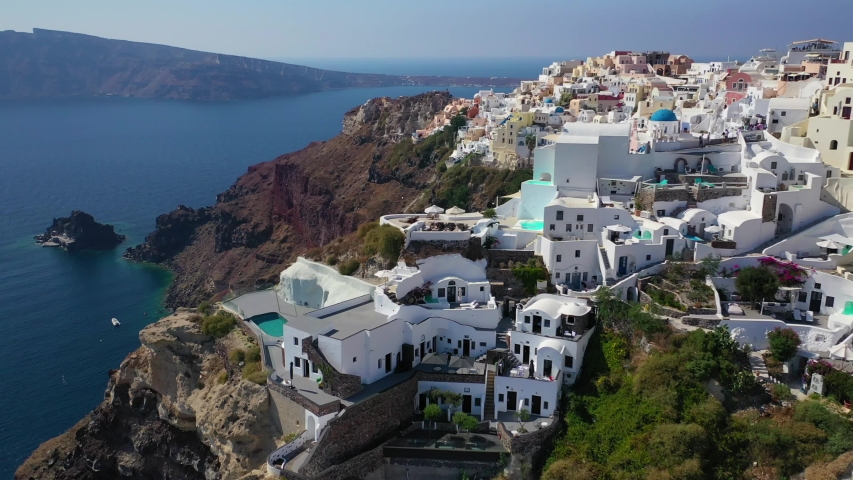Aerial drone video of famous whitewashed and colourful at the same time picturesque village of Oia built on a cliff, Santorini island, Cyclades, Greece