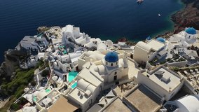 Aerial drone video of famous whitewashed and colourful at the same time picturesque village of Oia built on a cliff, Santorini island, Cyclades, Greece