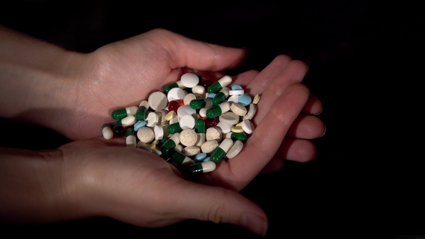 Close-up of person holding bunch of pills and capsules in his hands.Thumb interferes medication on black background.