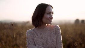 Outdoor slow motion video of young beautiful lady in autumn landscape with dry flowers. Knitted sweater. Warm Autumn day. brunette walking in park.