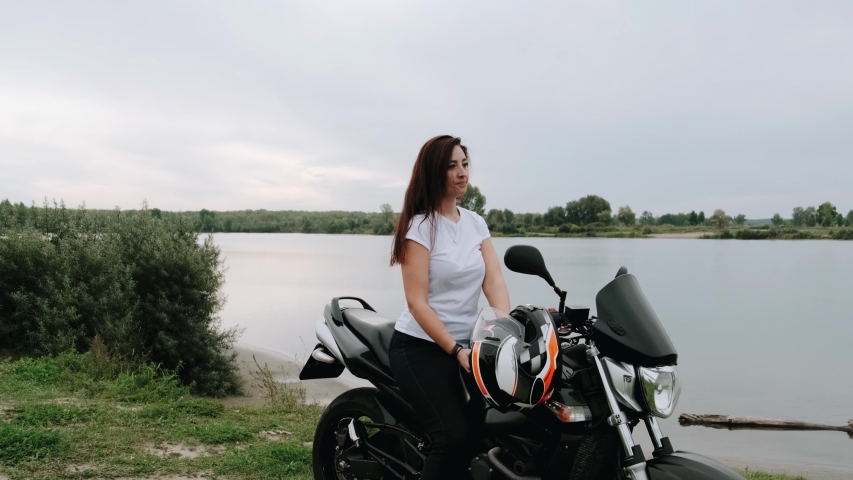 A girl sitting on a motorcycle puts on her leather jacket. Biker fastens leather jacket. 4k slow motion
