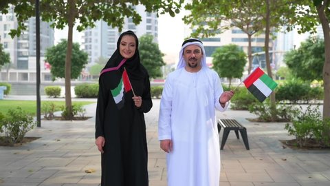 Arab couple holding UAE National Flag and gesturing the Dubai sign