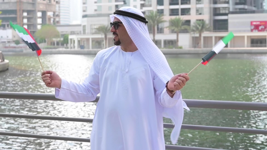 Arab man smiling while holding UAE flag in both hands