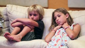 Candid kids seated on sofa watching TV screen