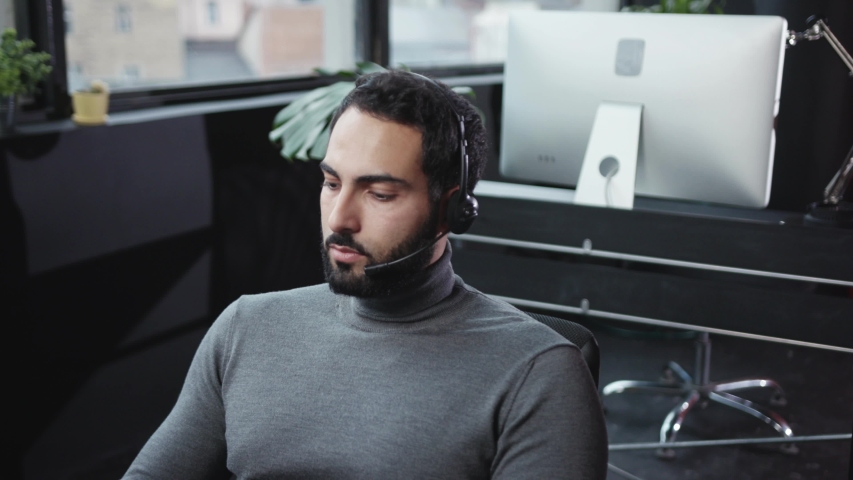 Male business manager wearing wireless microphone headset talking with client consulting with phone call working in customer service office.