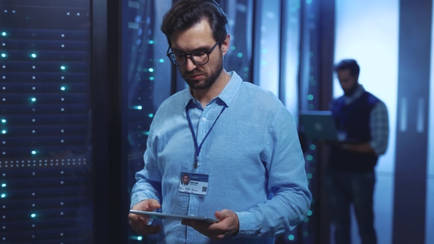 Modern server engineer working in IT company network and data center. Portrait of cheerful positive young man specialist with digital tablet in operative rack server room. | Shutterstock HD Video #1039683329