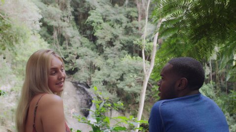 Millennial friends talking in front of small waterfall in an Australian rainforest by safety railing during daytime. Medium to closeup shot with camera zoom out on 4k RED camera.