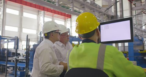 Two engineers white collars discussing with workman in uniform data at display of computer of CNC machine operation. Three colleagues have conversation at industrial background. Corporate