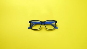 Human hands search, find and take eye glasses in blue plastic frame. On yellow background.