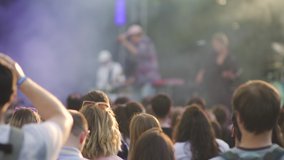 American people dance on rock concert, taking photo and video using smartphone. Back view of man and woman dancing, watching, doing photo holding mobile phone in hand. Crowd front of stage with smoke