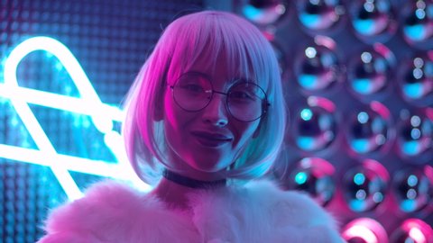 Portrait Beautiful Trendy 20s Girl In Glasses Looking At Camera and Smile. Confident and Elegant Woman with Open Eyes in Violet Blue Light Posing at Party. Cute Female Closeup in Colourful Pink Colors