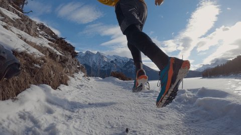Low angle shot trail runner exercising on snowy mountain trail. Man running on trail covered in snow