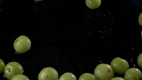 Emblica fruit pouring to water on black background slow motion