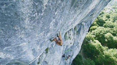 strong muscular man rock climber dynamically climbing on a limestone cliff, making several hard wide moves, gripping holds, and falling. outdoors rock climbing and active lifestyle concept, wide angle