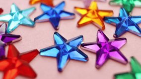 Rhinestones in the form of multi-colored stars on a pink background. Macro. The concept of a holiday, party, fun.