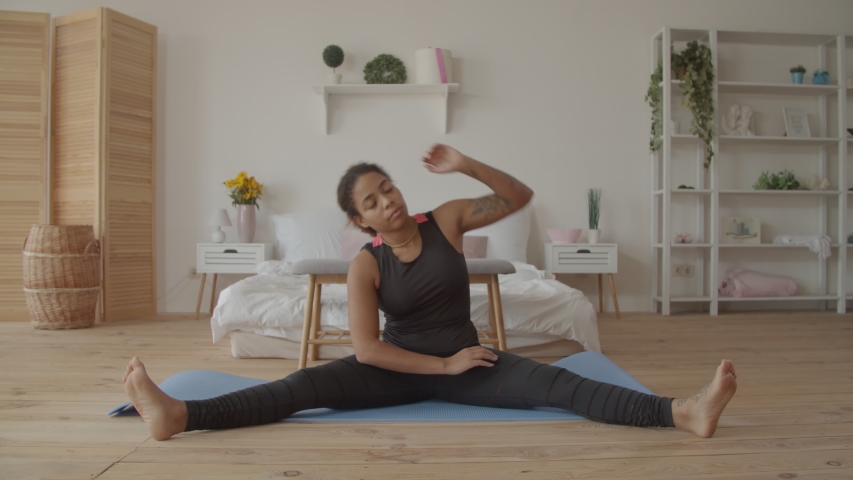 Active healthy lifestyle charming black woman warming up, doing side bending exercise on fitness mat at home. Sporty african american woman working out, practicing gymnastic exercise indoors. Royalty-Free Stock Footage #1039731287