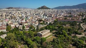 Aerial drone video of iconic Temple of Hephaestus in Ancient Forum of Athens historic centre and Lycabettus hill at the background, Attica, Greece