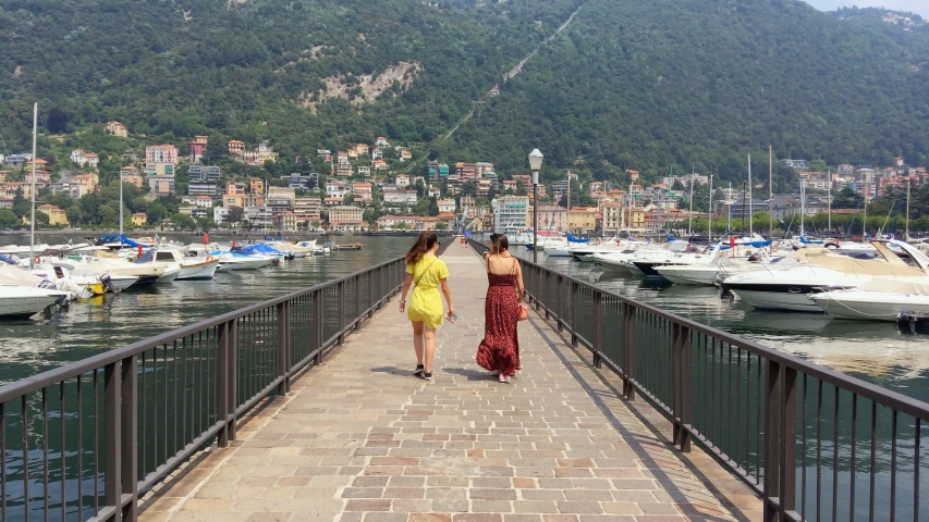 couple of girls walking on the long walkway of the Como lake. Camera following the scene