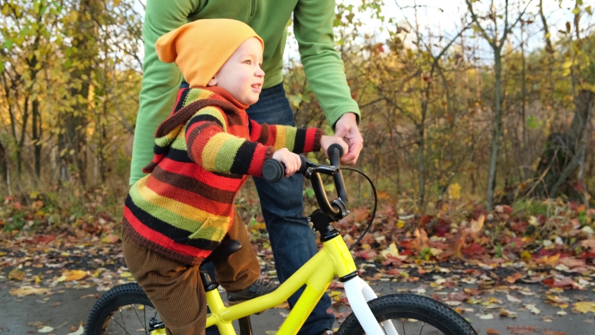 Father teaches his little child to ride bicycle in autumn park. Happy family moments. Time together dad and son. Candid lifestyle footage.  Royalty-Free Stock Footage #1039739789