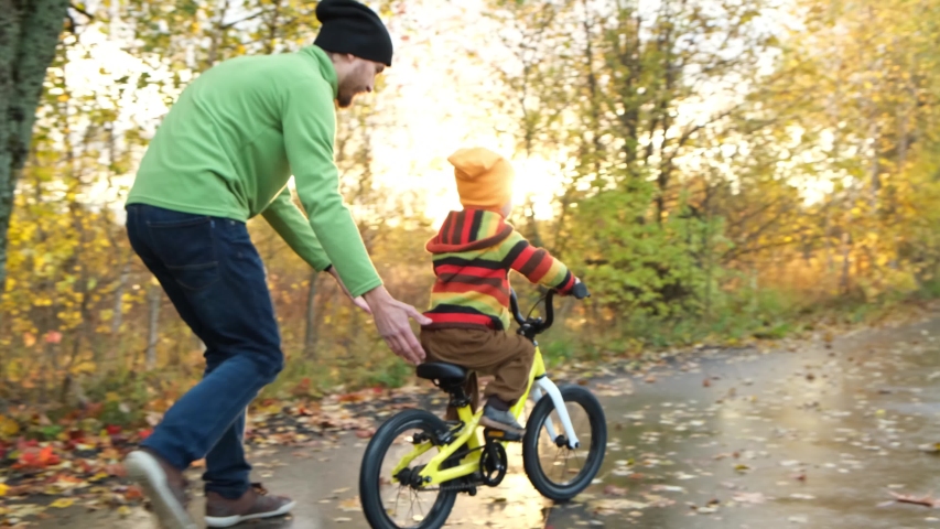 Father teaches his little child to ride bicycle in autumn park. Happy family moments. Time together dad and son. Candid lifestyle footage.  | Shutterstock HD Video #1039739789