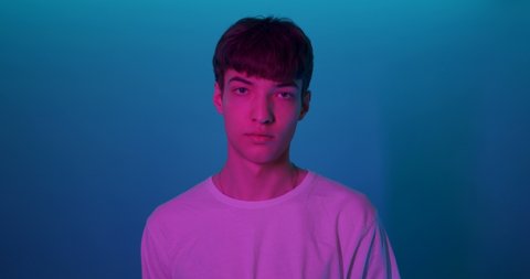 Portrait of Young Millenial Stylish Guy Wearing White T-Shirt Looking Straight to Camera Standing at Futuristic Neon Blue Lights. Lifestyle and People Concept.