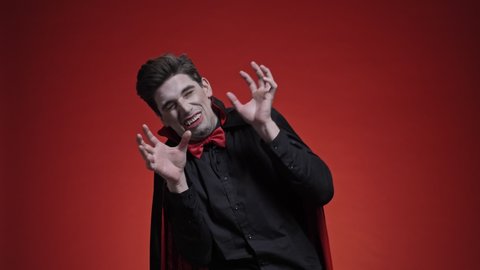 Sleeping man dracula with crossed hands in black halloween costume is being scared of light isolated over red wall