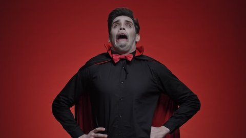 Vampire man with blood and fangs in black halloween costume is
sneezing isolated over red wall