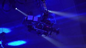 Video camera on the tap when shooting a television show. Live concert. The movement of the camera over the audience under the ceiling. Shooting from a height. Spotlights illuminate the scene. Blue
