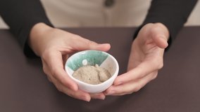 Close-up demonstration video of a woman's hands holding ceramic bowl with organic dried roots powder. Natural skin care. Homemade cosmetics preparation. Isolated, selective focus shot