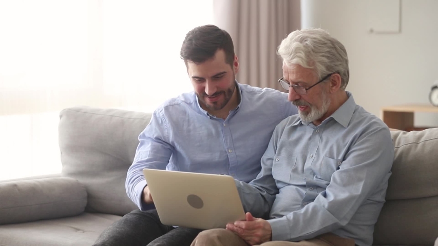 Different age generations men sixty years 60s elderly father millennial son sitting on couch having fun using internet websites laughing watching video on laptop, warm good intergenerational relations Royalty-Free Stock Footage #1039779347