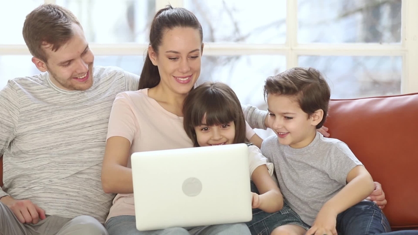Full family with two little kids daughter and son sitting on couch at home using laptop new apps, browsing internet, booking hotels planning future travel holiday, activities with modern tech concept Royalty-Free Stock Footage #1039785869