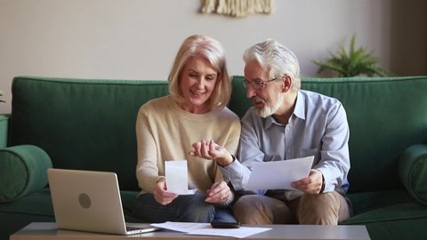 Smiling aged married couple sitting manage family budget check receipts loan contract conditions use e-banking, older generation online services modern tech easy usage, accounting, bookkeeping concept