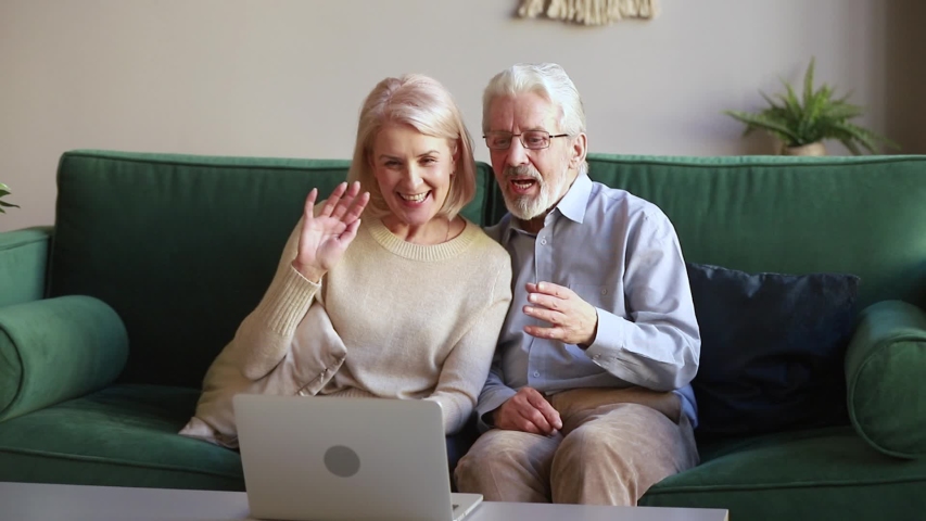 Elderly spouses sit on couch in living room country house make videocall look at pc screen wave hands greeting friend or grown up children grandchildren, modern tech and older generation users concept Royalty-Free Stock Footage #1039788470