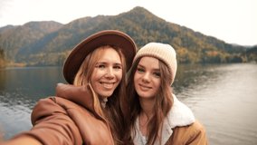 two attractive girls young women fashionably dressed on vacation on a lake in the mountains shoot video chat, selfie. the view from the camera. lesbian love. concept, advertising, friends