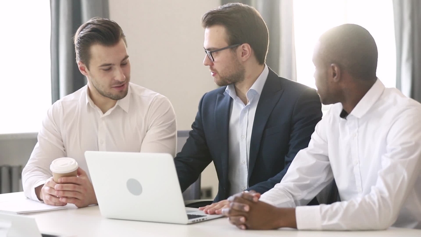 Three young office workers multi racial businessman sitting at desk discuss new profitable project, having informal talk listen team leader mentor, multi-ethnic employees friendship teamwork concept Royalty-Free Stock Footage #1039793726