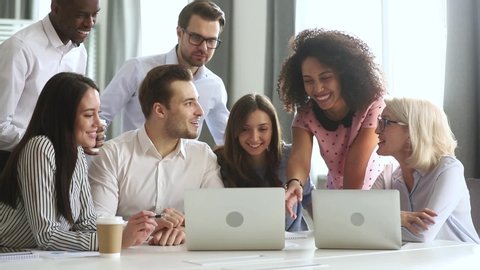 Multi racial employees gathered together in boardroom or co-working space listening mixed race millennial female team leader showing on laptop new software explain program or shares sales growth sales