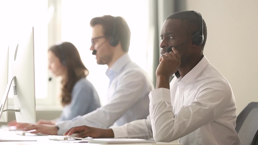 Call center diverse employees working in shared desk focus on african worker wearing headset typing look at pc screen talk help to company client distantly, provide information helpline office concept Royalty-Free Stock Footage #1039793777